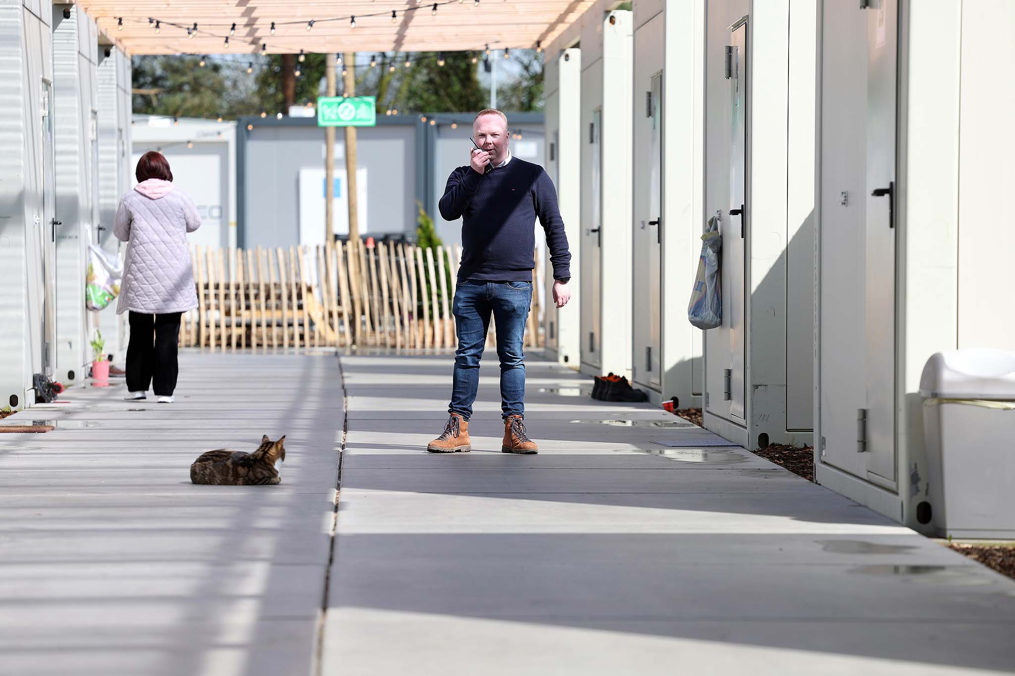 Man en vrouw op een overdekt pad tussen witte units, met een kat op de voorgrond