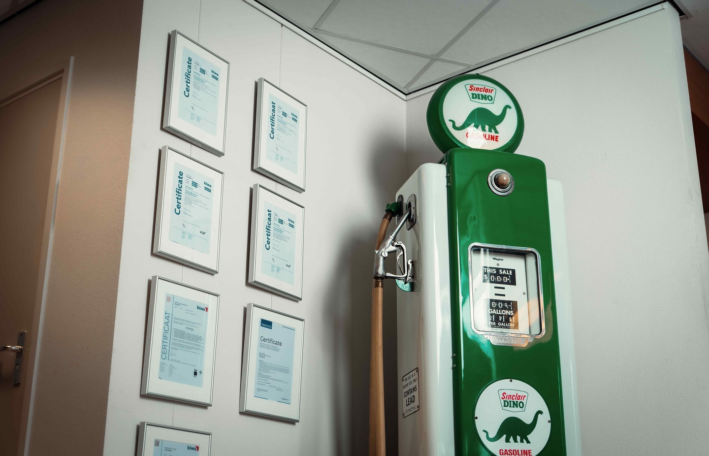 Ingelijste certificaten aan een muur naast een groene vintage benzinepomp