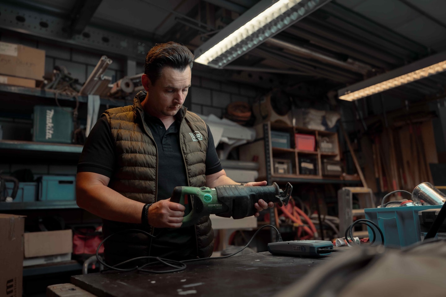 Man in bodywarmer met een elektrische zaag in een werkplaats