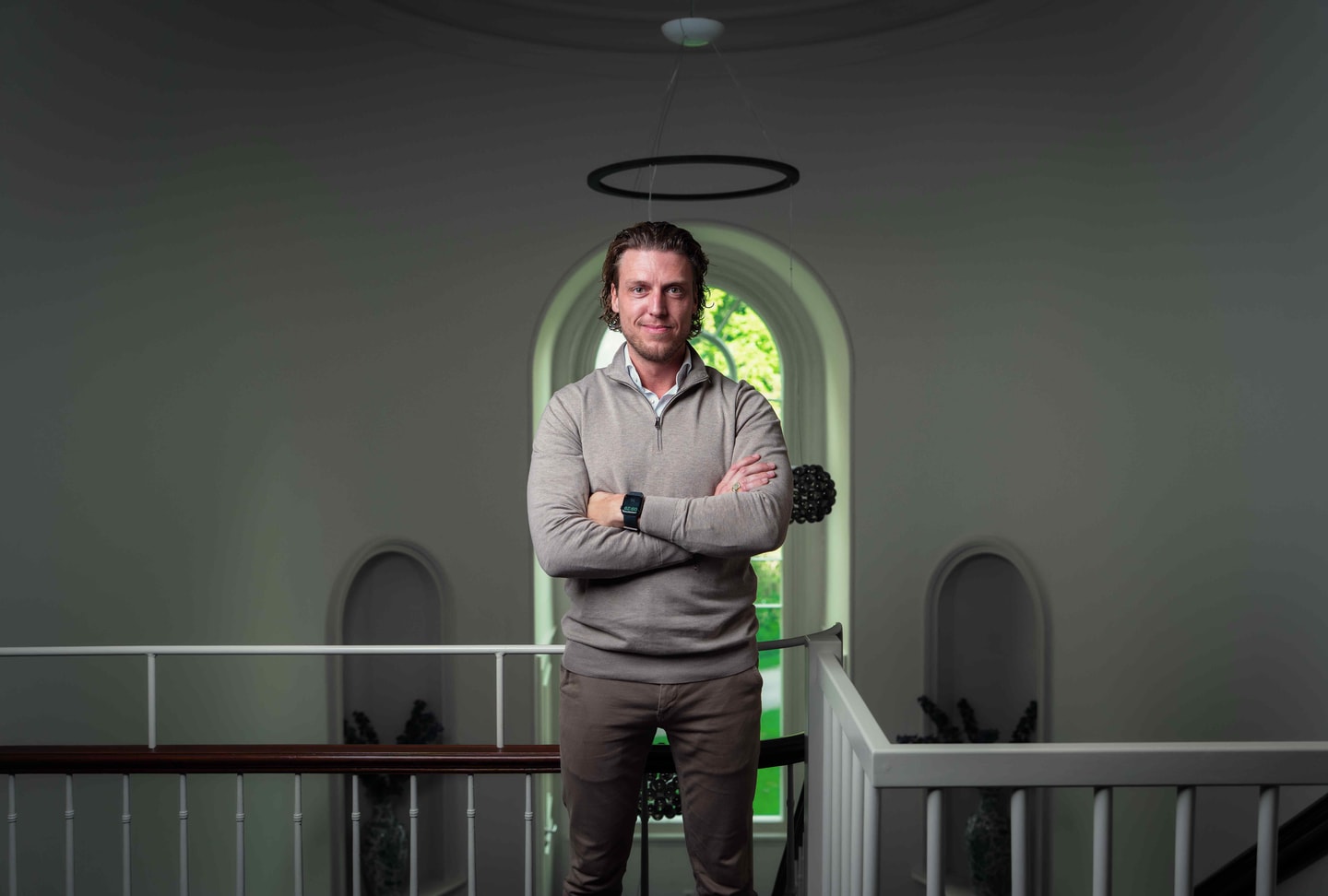 Roy Diks met de armen over elkaar onder een boogvormige doorgang in een witte hal