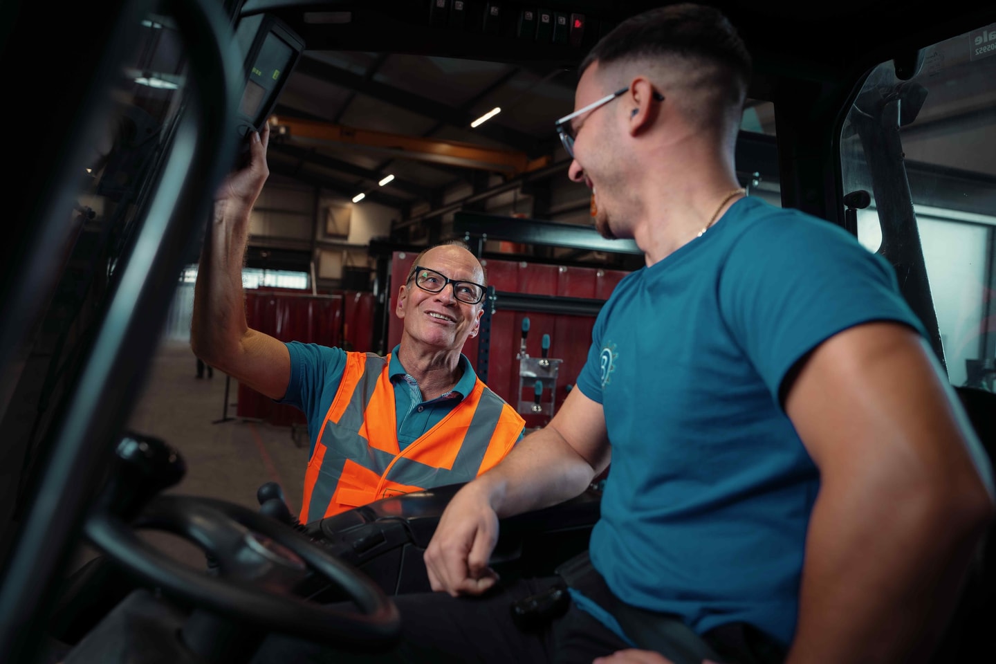 Lachende adviseur in oranje hesje praat met een heftruckchauffeur in een productiehal