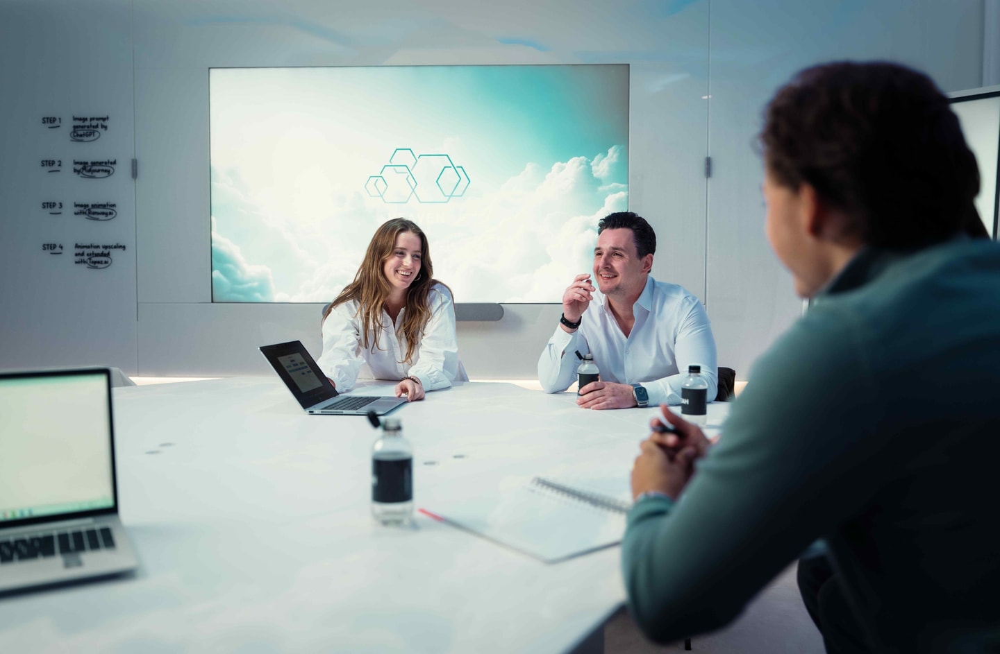 Drie mensen in overleg aan een witte vergadertafel met een groot scherm aan de wand