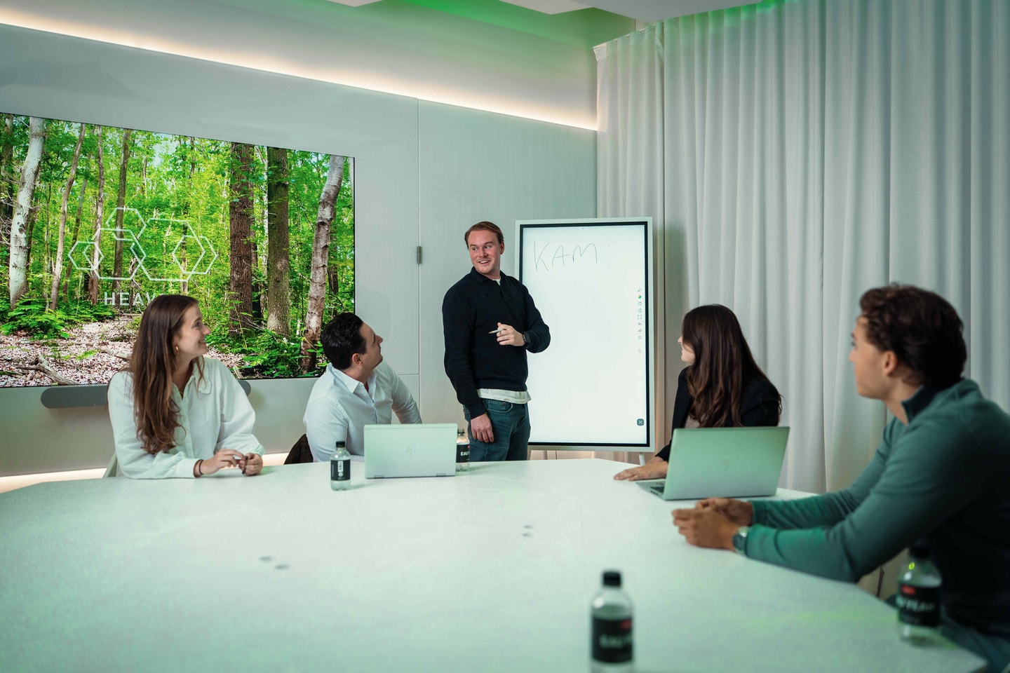 Vergadering met laptops aan een lichte tafel voor een fotowand met bomen
