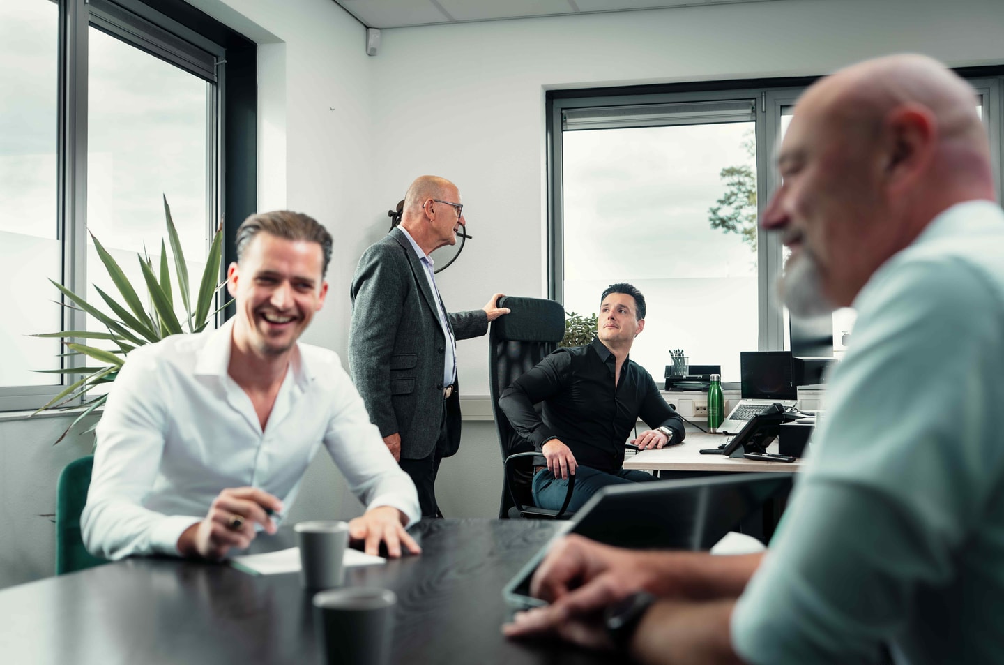 Lachende man aan een bureau in een kantoor, met collega’s achter hem