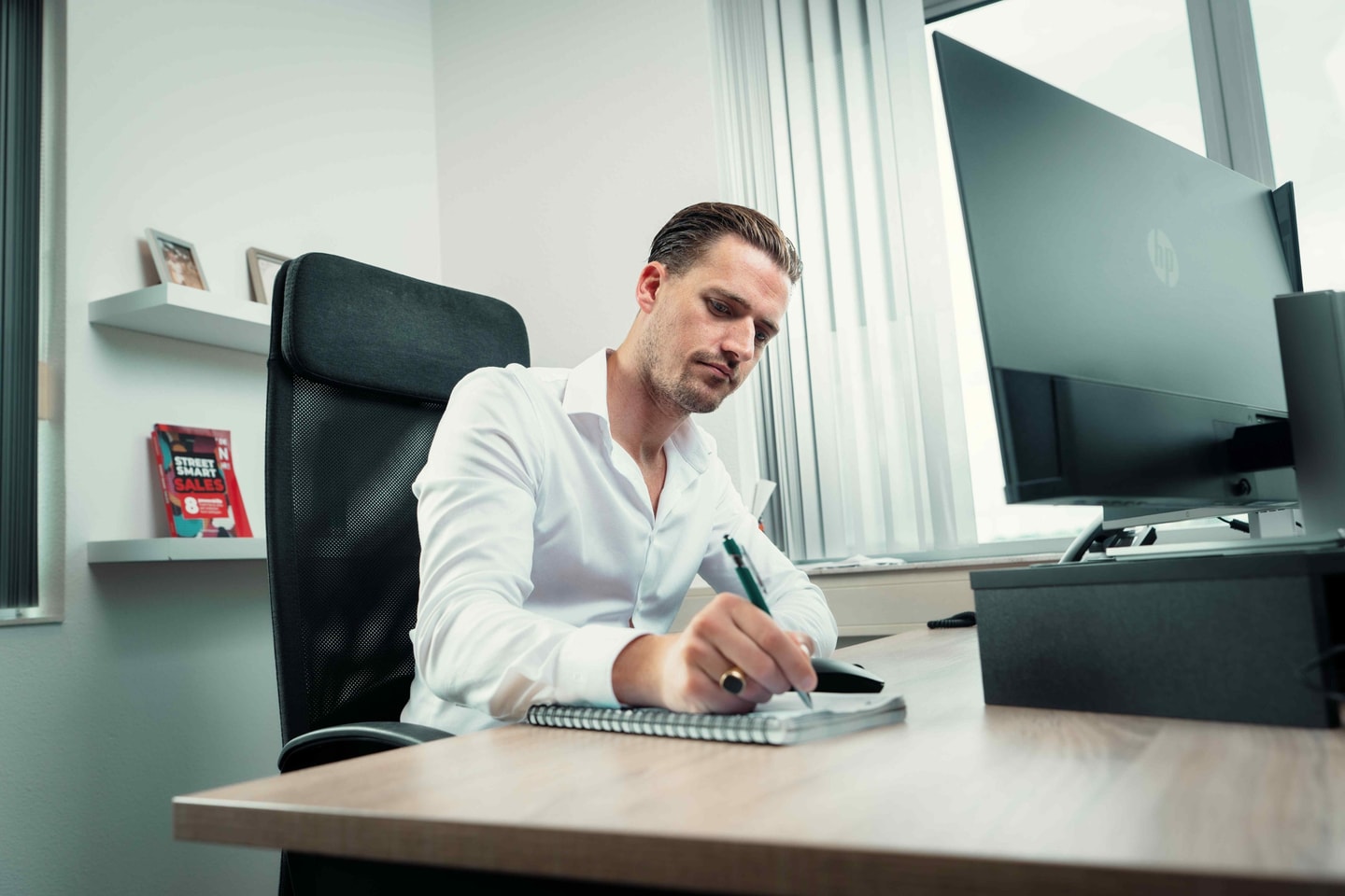 Man in wit overhemd schrijft in een notitieboek aan een bureau