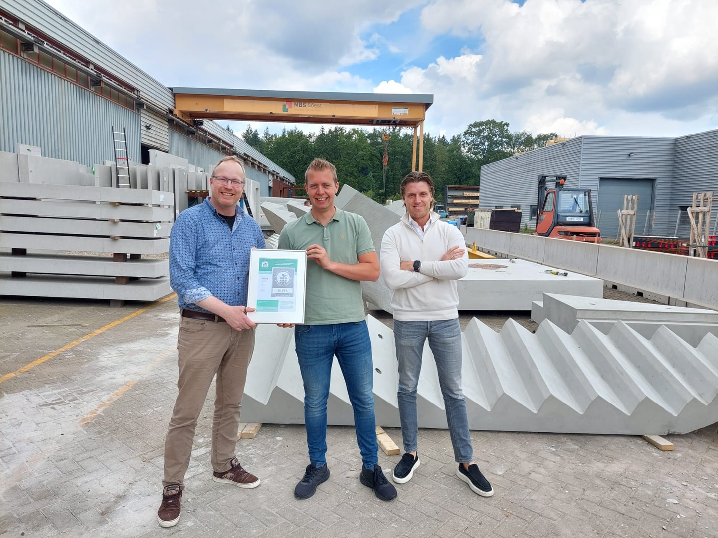 Drie mannen met een certificaat op een terrein met betonnen trapelementen