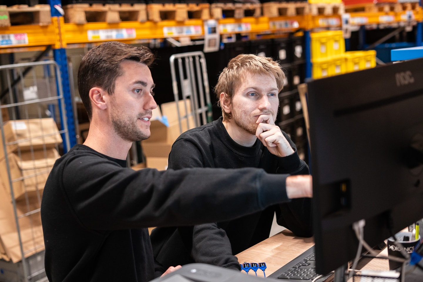 Twee mannen kijken naar een beeldscherm in een magazijn met stellingen