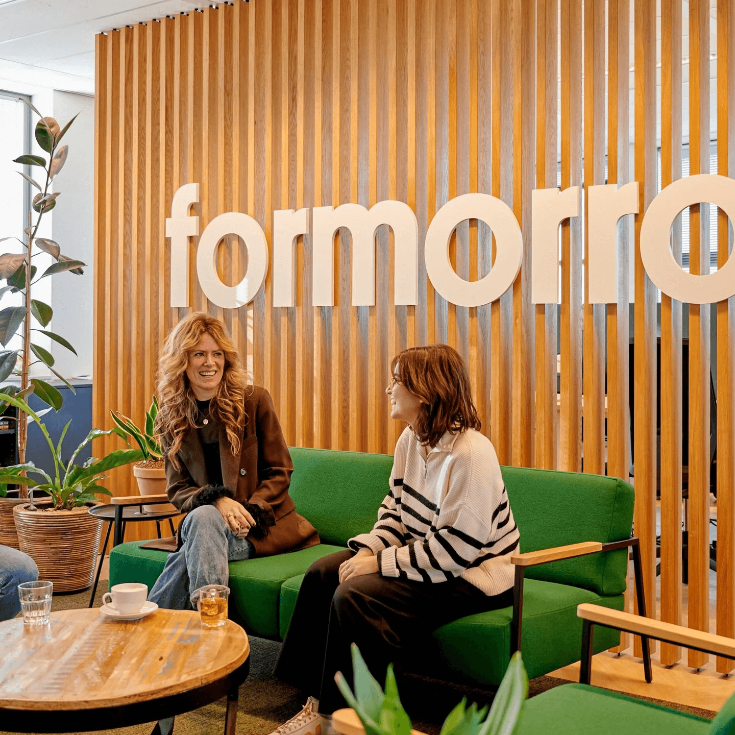 Twee vrouwen in gesprek op een groene bank voor een houten wand met de naam formorrow