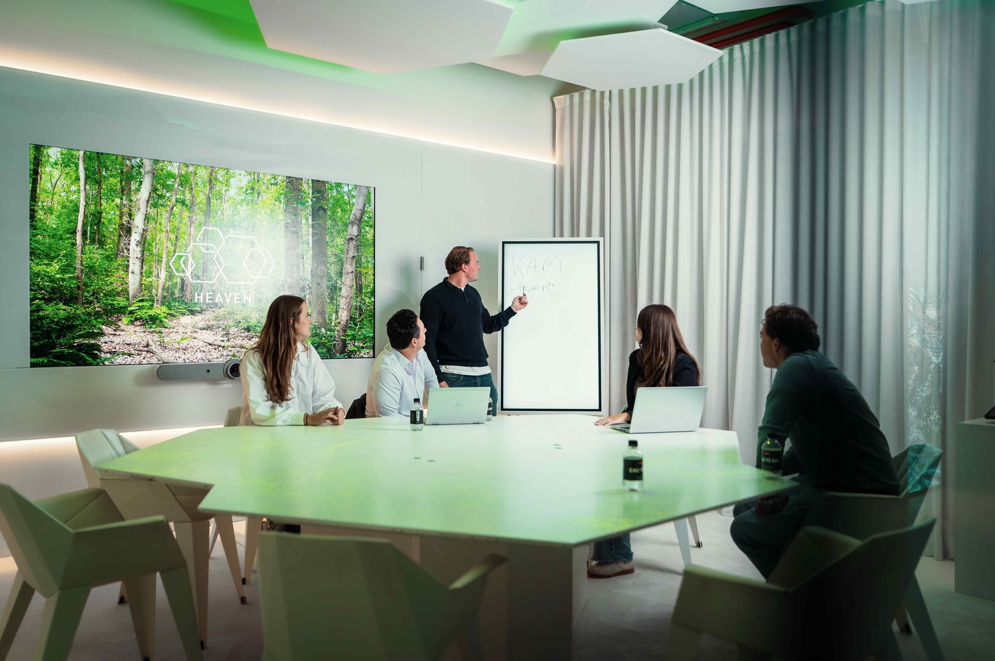 Overleg aan een lichte vergadertafel, een man schrijft op een whiteboard