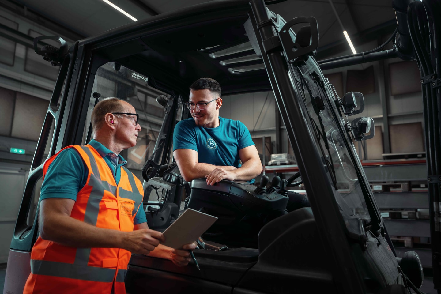 Man in een oranje veiligheidshesje overlegt met een heftruckchauffeur in de cabine