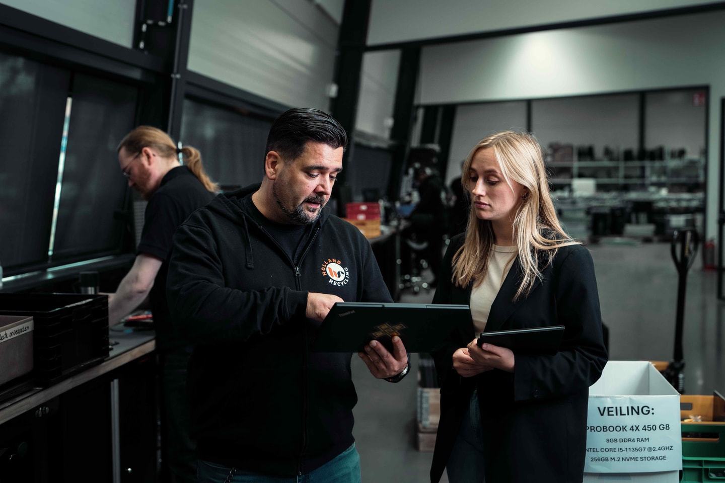 Drie mensen in een magazijn met elektronica bekijken samen een tablet